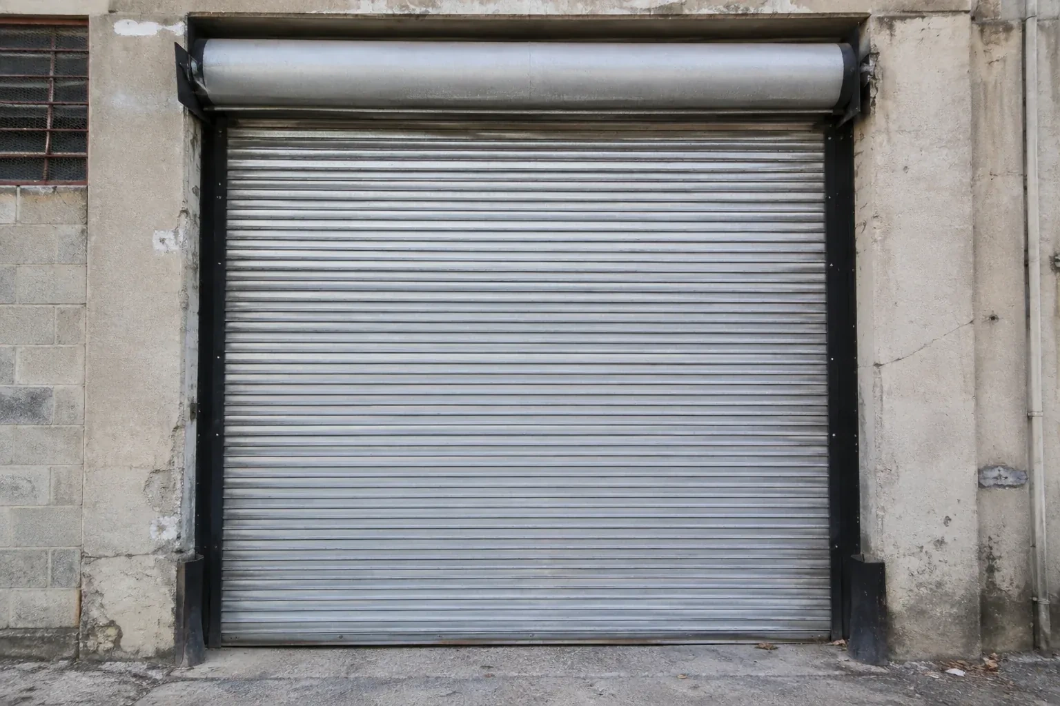 Closed metal rolling shutter in a weathered warehouse opening. — Commercial Rolling Door Repair, Toronto